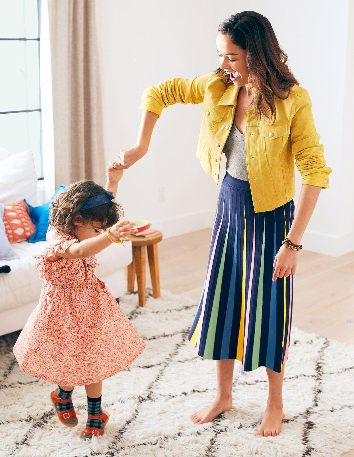 brunette mother twirling young daughter on rug in living room