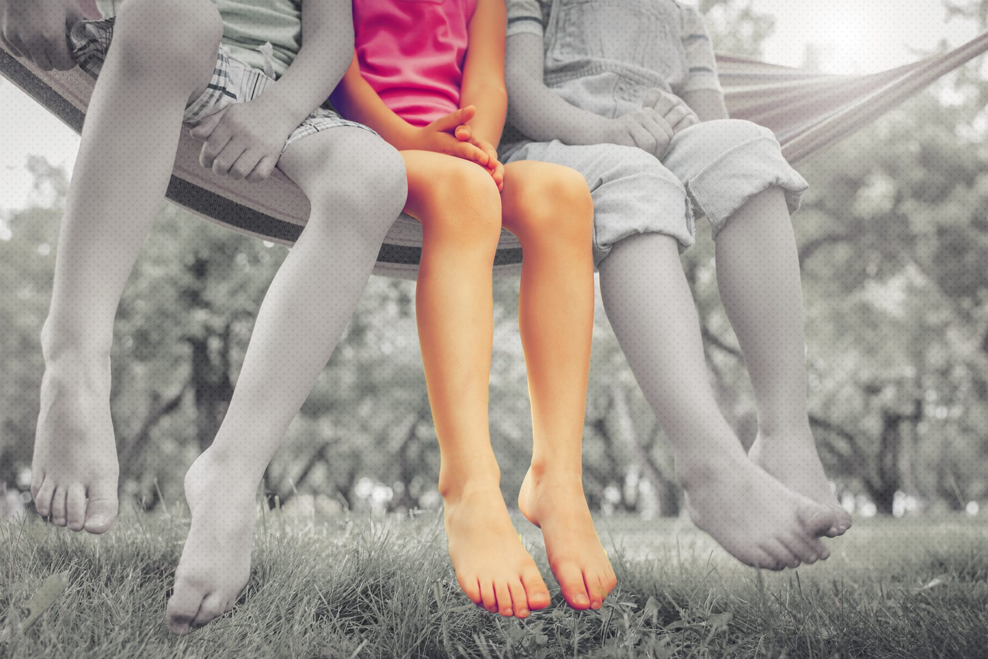 low angle of 3 kids sitting on hammock in black and white, middle child in full color