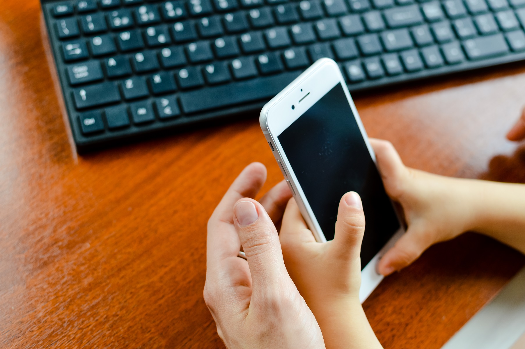 Adult and Child Hold Cell Phone iPhone Black Keyboard In Background