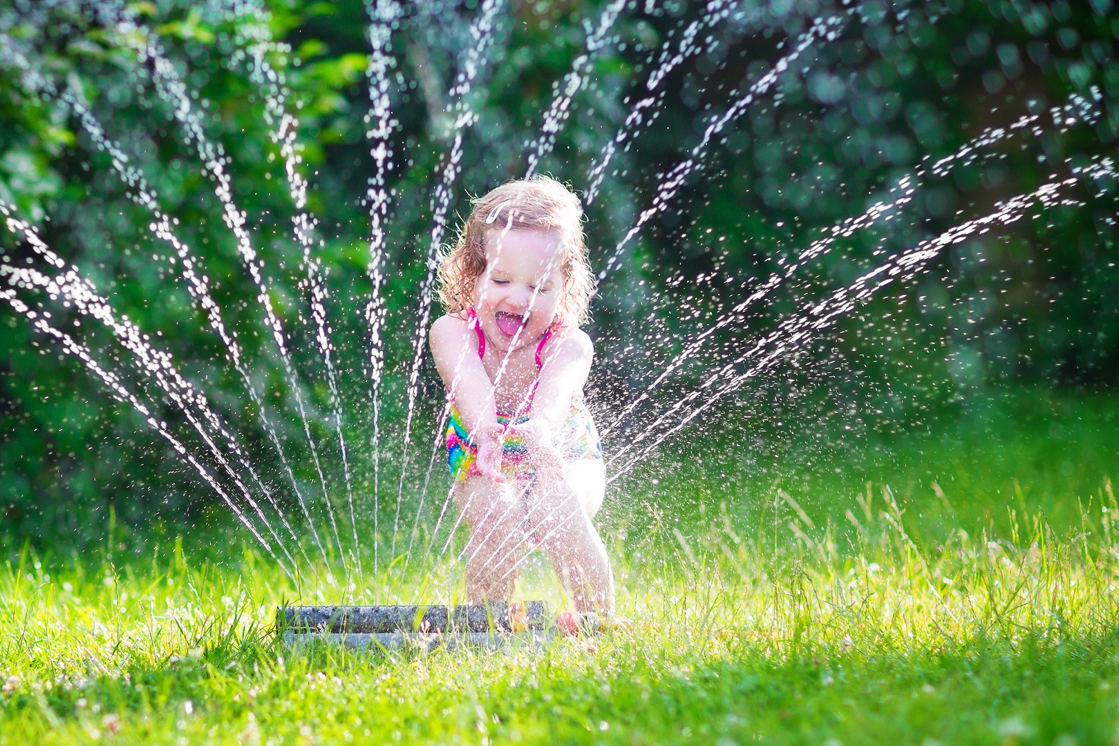 Little Girl Playing in Sprinkler Green Grass