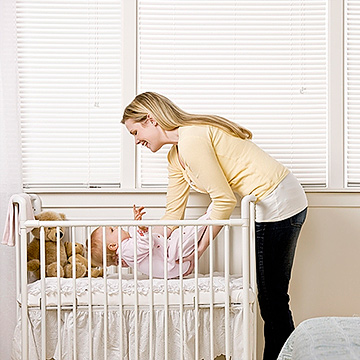 mother putting baby in crib